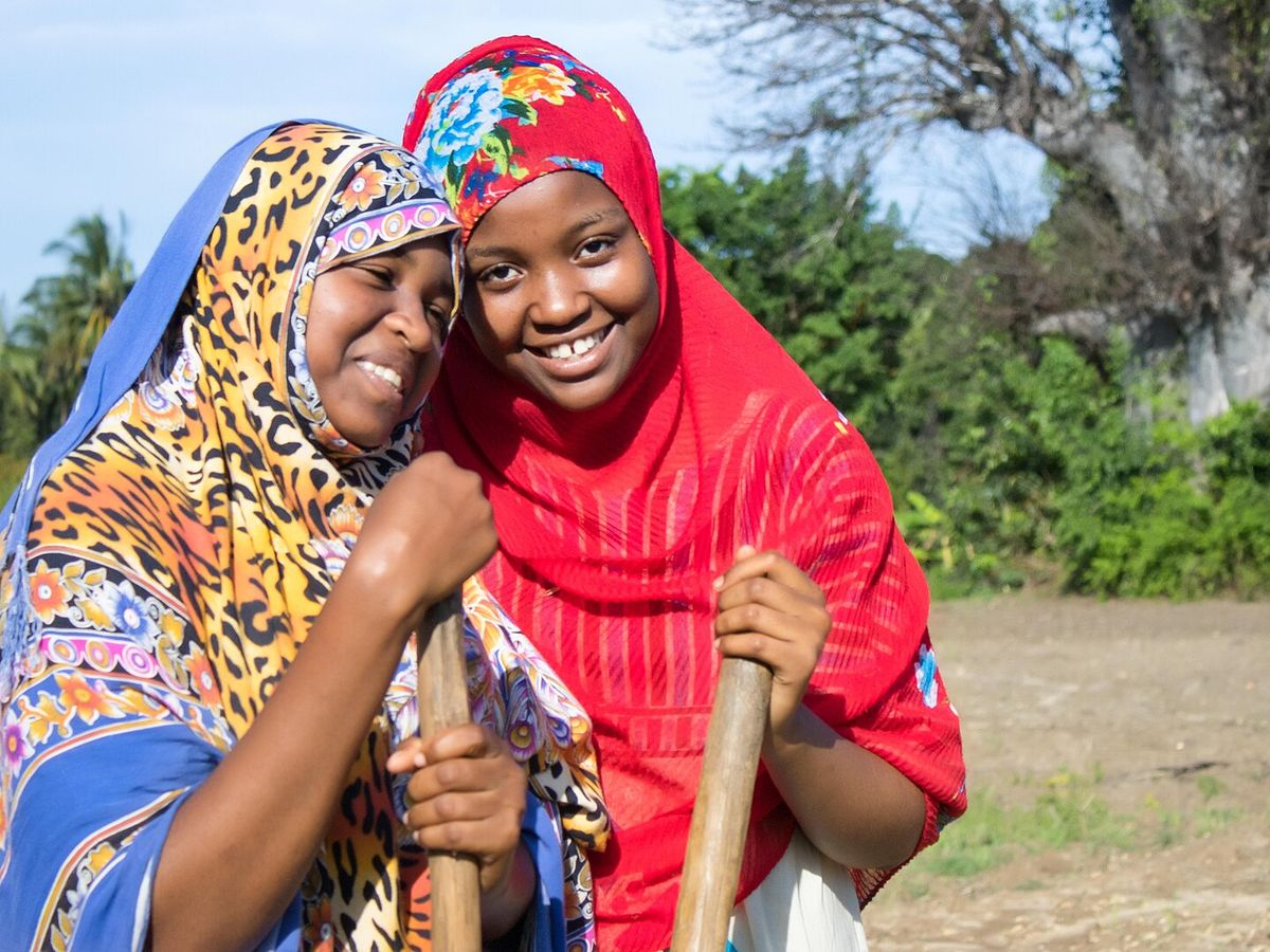 Two women standing together outdoors in a Tanzanian village, smiling